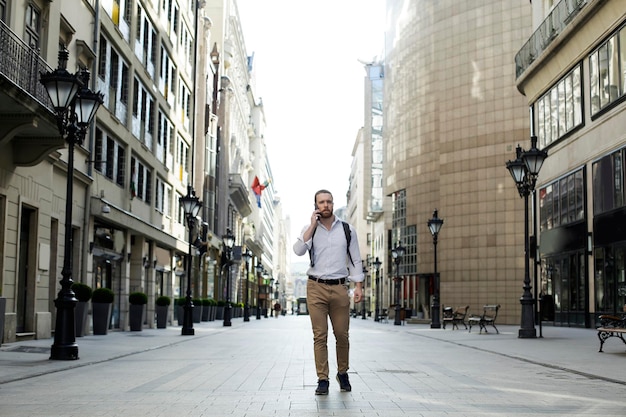 Portret mężczyzny rozmawiającego przez telefon komórkowy na ulicy pośród budynków w mieście