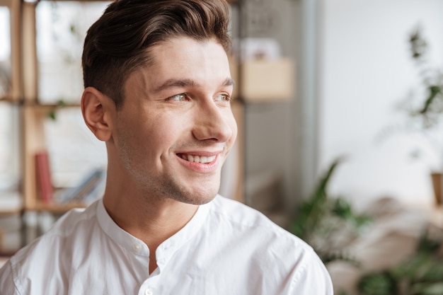 Portret mężczyzny ubranego w białą koszulę stojącego w pomieszczeniu. Coworking. Patrząc na bok.