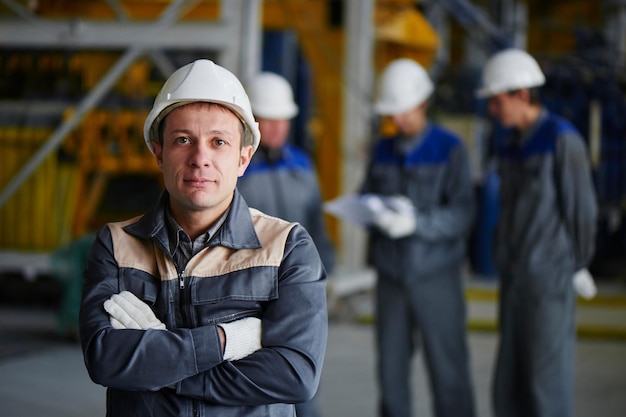 Portret mężczyzny w kombinezonie i kasku na tle grupy pracowników w budynku fabryki