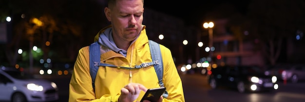 Portret mężczyzny z plecakiem używającego telefonu komórkowego na nocnej ulicy, rozmawiającego z przyjaciółmi, wzywającego taksówkę i sprawdzającego geolokalizację na mapie