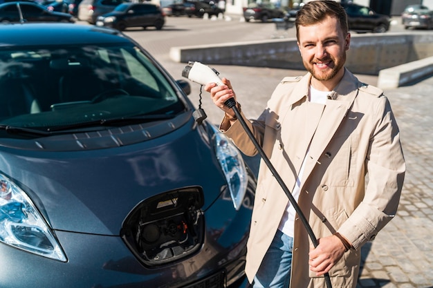 Portret mężczyzny ze złączem ładowania samochodu elektrycznego w rękach