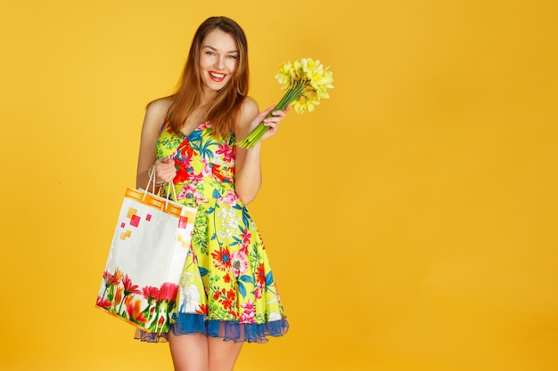 Portret młoda szczęśliwa uśmiechnięta kobieta z torba na zakupy przeciw kolor żółty ścianie