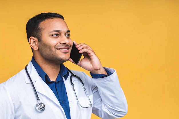 Portret Młodego African American Indian Black Man Lekarz Na Białym Tle Nad żółtym Tle, Rozmawiając Na Smartfonie, Uśmiechając Się Pozytywnie. Korzystanie Z Telefonu Komórkowego.