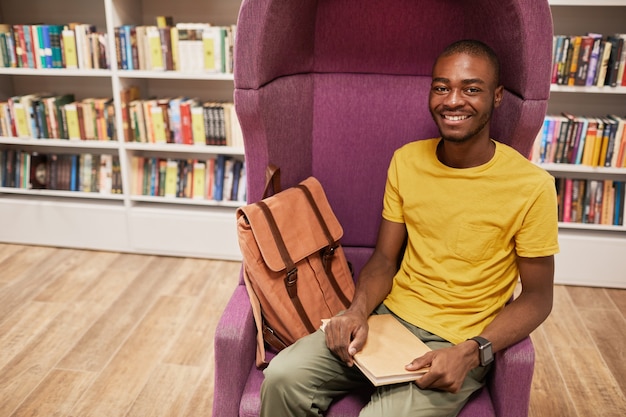 Portret młodego afrykańskiego studenta patrzącego na kamerę podczas nauki w szkolnej przestrzeni kopii biblioteki