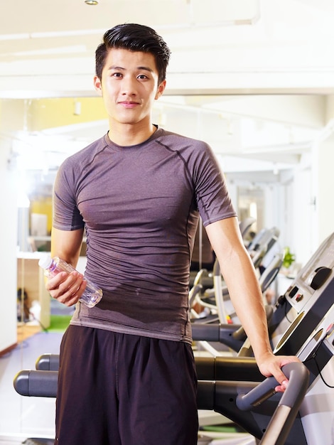 Portret młodego azjatyckiego mężczyzny trzymającego butelkę wody w siłowni