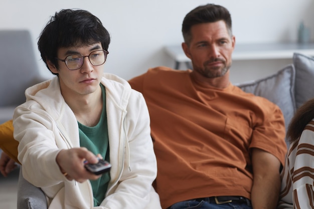 Portret młodego azjatyckiego mężczyzny trzymającego pilota telewizora podczas oglądania filmów z przyjaciółmi i rodziną w domu