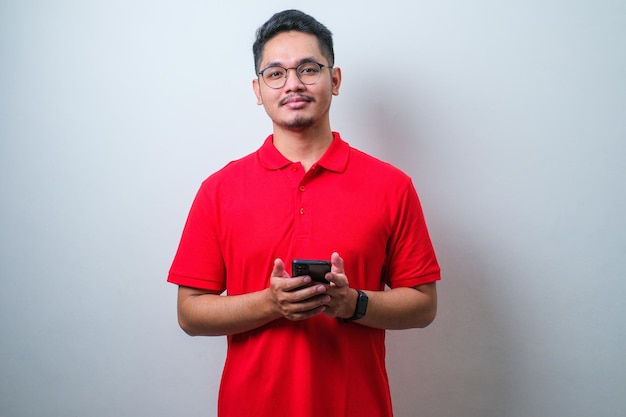 Portret młodego azjatyckiego mężczyzny w dorywczo czerwonej koszuli za pomocą smartfona handlującego lub rozmawiającego