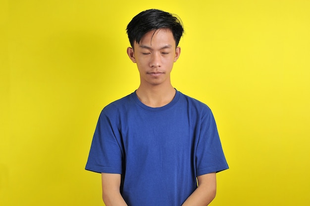 Portret młodego azjatyckiego mężczyzny zamyka oczy, odizolowane na żółtym tle