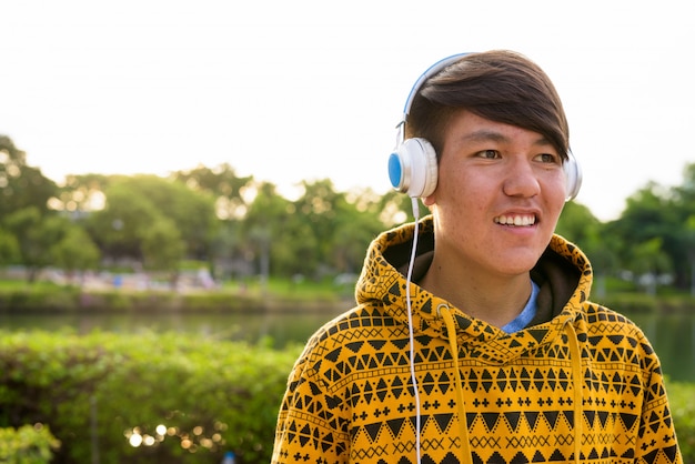 Portret młodego azjatyckiego nastoletniego chłopca na sobie bluzę z kapturem i słuchawki podczas relaksu w parku w Bangkoku w Tajlandii