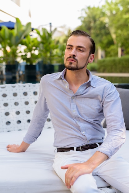 Portret młodego brodaty modny mężczyzna siedzi na zewnątrz