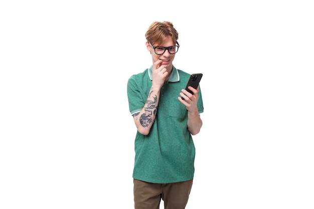 Portret młodego czerwonowłosego faceta w zielonej koszulce myśląco czytającego wiadomości na smartfonie