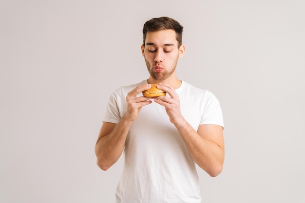 Portret młodego głodnego mężczyzny z jedzeniem pysznego burgera na białym tle na białym tle