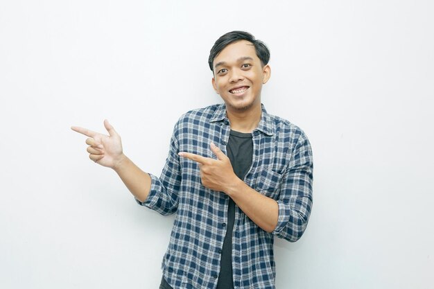 Zdjęcie portret młodego indonezyjskiego mężczyzny azjatyckiego uśmiechającego się i palca wskazującego na lewą stronę ze szczęśliwym wyrazem niebieska flanelowa koszula i czarna koszula