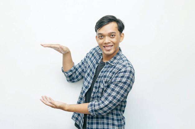 Zdjęcie portret młodego indonezyjskiego mężczyzny azjatyckiego uśmiechającego się, kładąc ręce z boku ciała, aby przedstawić coś gestem