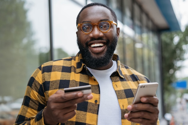 Portret młodego mężczyzny Afroamerykanów uśmiechnięta posiadania karty kredytowej, zakupy w Internecie