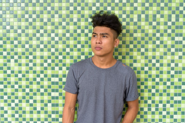 Portret młodego mężczyzny Azji z kręconymi włosami na zielonej ścianie kaflami
