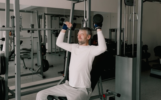 Portret młodego mężczyzny ćwiczeń fizycznych, treningu z hantlami, siedzącego na ławce w siłowni. W białej koszulce. zdrowy tryb życia