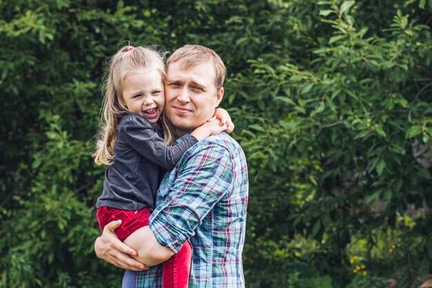 Portret Młodego Mężczyzny I Małej Dziewczynki Przytulających Ojca Na Letnim Trawniku W Ciepły Letni Dzień, Szczęśliwe Ojcostwo