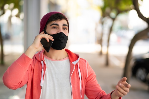 Portret młodego mężczyzny rozmawia przez telefon podczas spaceru na ulicy. Człowiek sobie maskę na twarz. Koncepcja miejska.