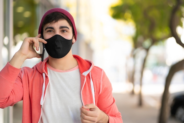 Portret młodego mężczyzny rozmawia przez telefon podczas spaceru na ulicy. Człowiek sobie maskę na twarz. Koncepcja miejska.