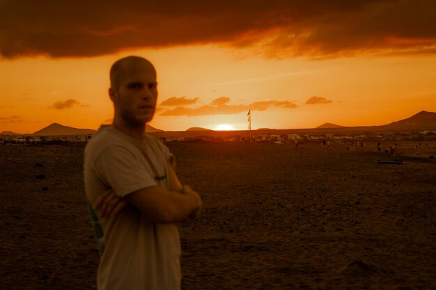 Portret młodego mężczyzny stojącego na plaży na tle nieba podczas zachodu słońca