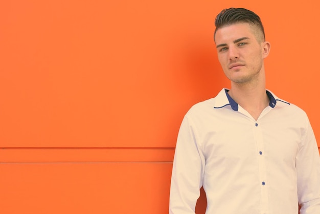 Zdjęcie portret młodego mężczyzny stojącego przy pomarańczowej ścianie