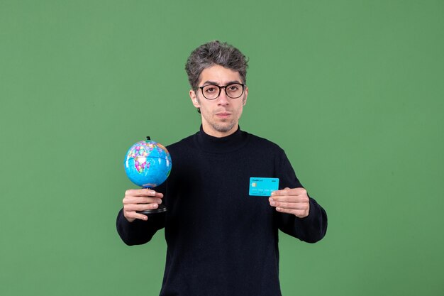 portret młodego mężczyzny trzymającego kulę ziemską i kartę kredytową zielone tło męski bank pieniędzy natura