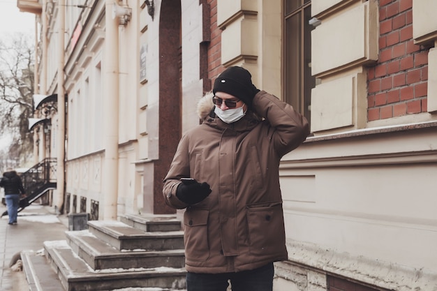 Portret młodego mężczyzny w swobodnych zimowych ubraniach z okularami i maską medyczną na spacer po mieście