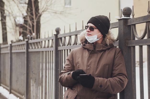 Portret młodego mężczyzny w swobodnych zimowych ubraniach z okularami i maską medyczną na spacer po mieście