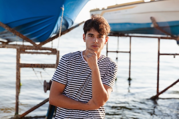 Portret Młodego Mężczyzny W T-shirt W Paski, Przebywającego Na Tle łodzi Na Morzu.