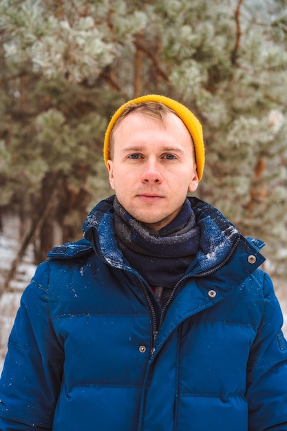 Portret młodego mężczyzny w żółtym kapeluszu w śnieżnym zimowym lesie, święta Bożego Narodzenia