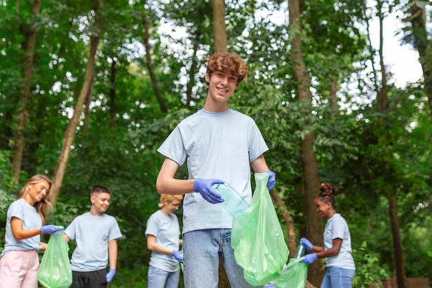Zdjęcie portret młodego mężczyzny z małą grupą wolontariuszy na tle z rękawiczkami i workami na śmieci, sprzątanie parku miejskiego, ochrona środowiska i koncepcja ekologii, wszystko na sobie niebieskie koszulki