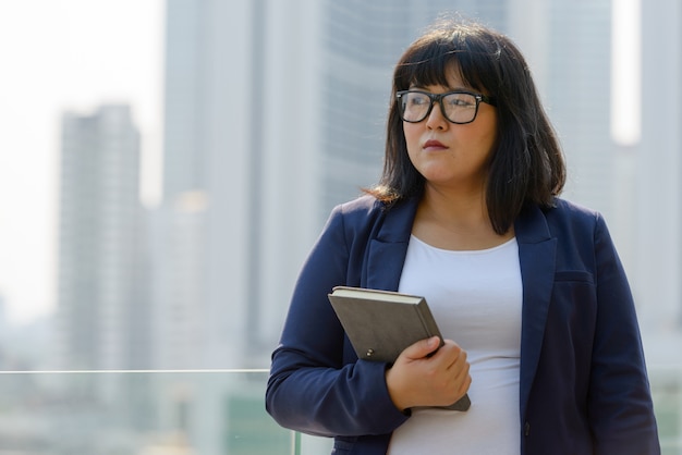 Portret młodego pięknego azjatyckiego bizneswoman z nadwagą z widoku na miasto