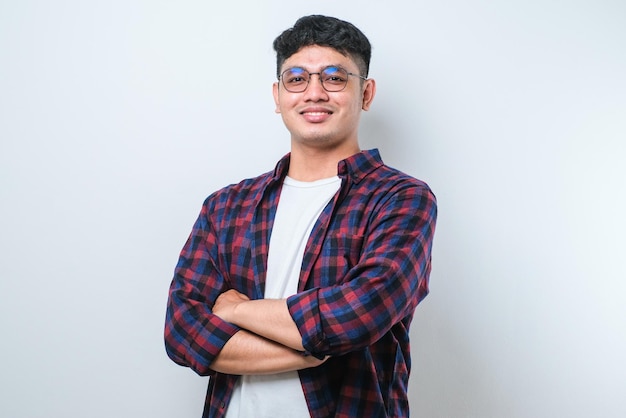 Portret młodego przystojnego azjatyckiego mężczyzny w casualowej koszuli i okularach, stojącego ze skrzyżowanymi rękami i uśmiechającego się do kamery