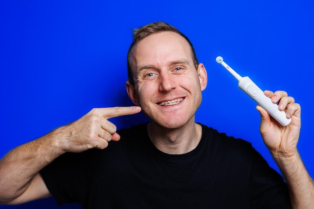 Portret młodego przystojnego mężczyzny myjącego zęby ultradźwiękową nowoczesną szczoteczką do zębów Pielęgnacja jamy ustnej Poranna samoopieka