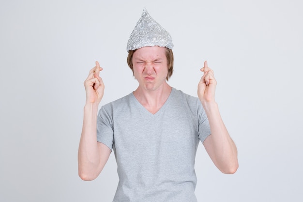 Zdjęcie portret młodego przystojnego mężczyzny na sobie kapelusz z folii aluminiowej jako koncepcja teorii spiskowej na białym tle