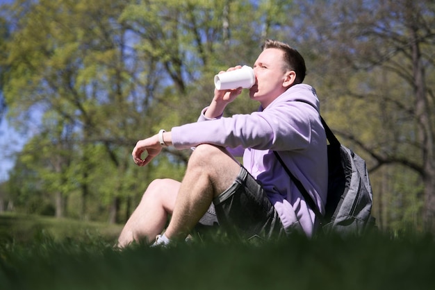 Portret młodego przystojnego mężczyzny pijącego kawę w mieście z filiżanki w letni dzień kawa na wynos