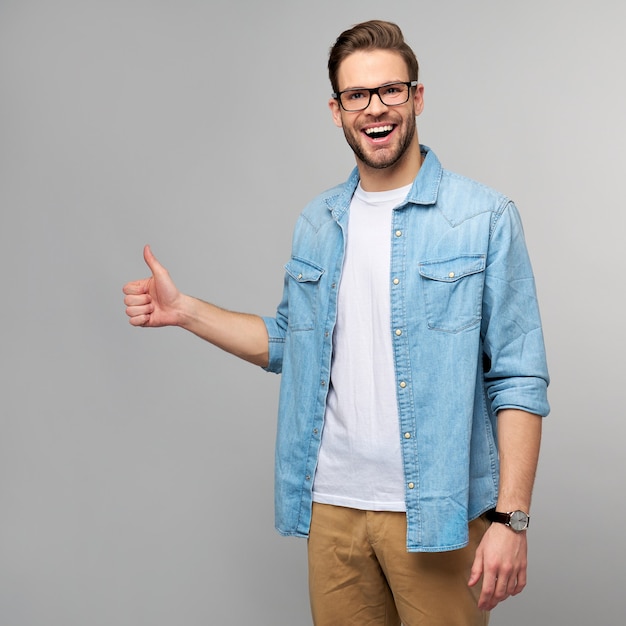 Portret młodego przystojnego mężczyzny w koszuli dżinsy Wyświetlono duży kciuk gest stojący nad ścianą