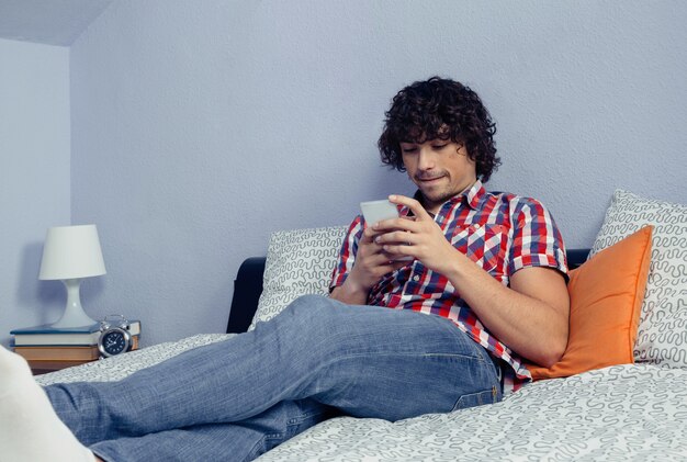 Portret Młodego Przystojny Mężczyzna Patrząc Smartphone I Odpoczynek Nad łóżkiem. Czas Wolny W Koncepcji Domu.