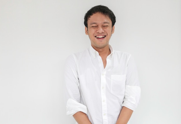 Portret młodego śmiesznego azjatyckiego mężczyzny z białą koszulą, patrząc na kamerę i uśmiechniętego, szczęśliwego wyrażenia