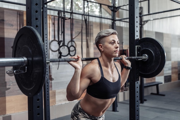 Portret młodego sportowca muskularna kobieta ze sztangą na ramionach w nowoczesnej siłowni krzyżowej. Sport, koncepcja fitness