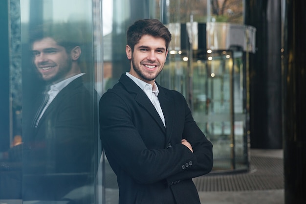 portret młodego szczęśliwego biznesmena ubranego w oficjalną odzież stojącego w pobliżu centrum biznesowego