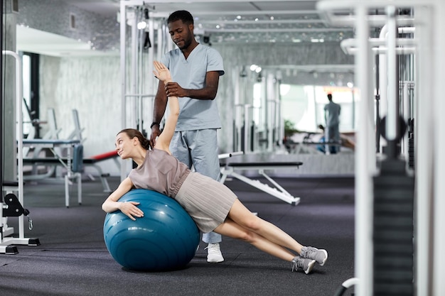 Portret młodego terapeuty pomagającego kobiecie w wykonywaniu ćwiczeń fitness w klinice rehabilitacyjnej kopia przestrzeń