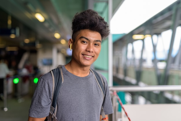 Portret młodego turysty z Azji z kręconymi włosami jako tracoronavirus backpacker na stacji kolejowej w niebie