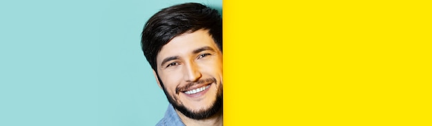 portret młodego uśmiechniętego faceta między dwiema ścianami kolorów żółtego i aqua menthe