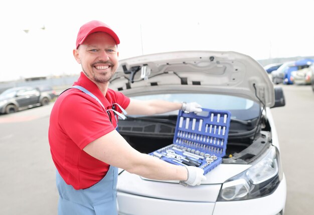 Portret młodego uśmiechniętego mechanika samochodowego z zestawem narzędzi na masce samochodu