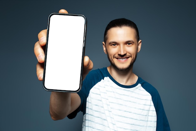 Portret młodego uśmiechniętego mężczyzny trzymającego smartfon z makietą na niebieskim tle