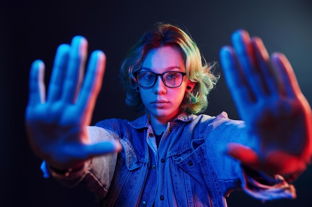 Portret młodej alternatywnej dziewczyny w okularach z zielonymi włosami w czerwonym i niebieskim świetle neonowym w studio