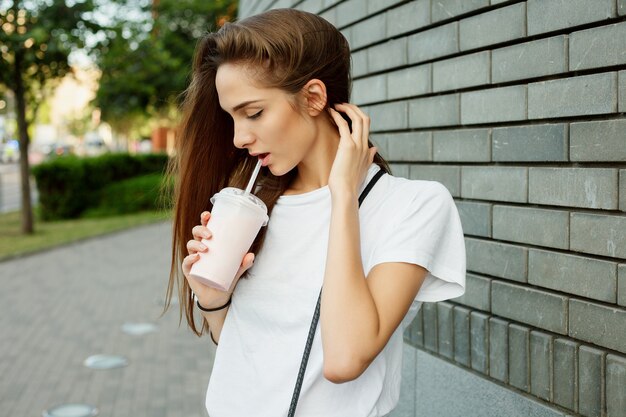 Portret młodej atrakcyjnej brunetki dziewczyny pijącej koktajl mleczny