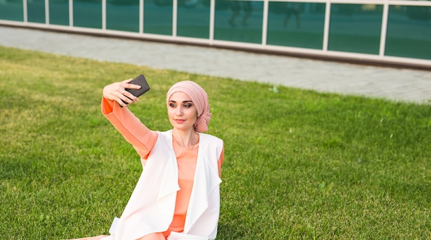 Portret młodej atrakcyjnej kobiety w hidżabie robi zdjęcie selfie na smartfonie w parku